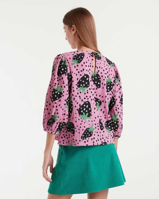 Woman wearing a pink blouse with strawberry pattern and green skirt on a white background