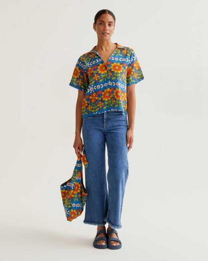 Woman wearing a colorful floral blouse and blue jeans holding a matching bag on a white background