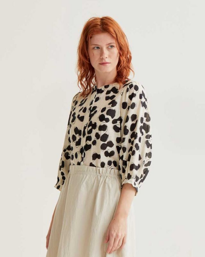 Woman wearing a leopard print top and beige skirt on a white background