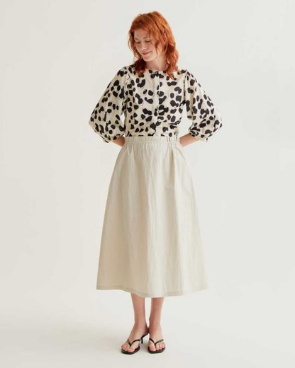 Woman wearing a leopard print blouse and beige skirt on a white background