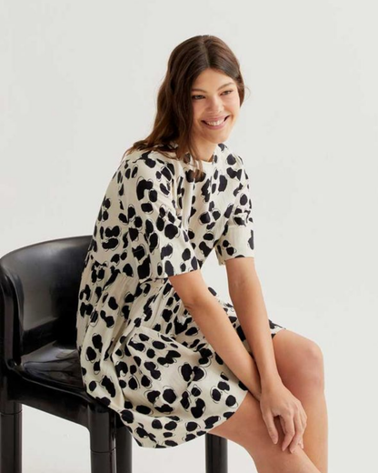 Woman wearing a leopard print dress sitting on a black chair against a white background