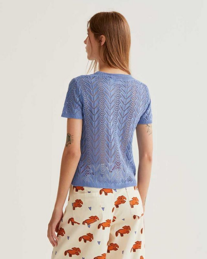 Woman wearing a blue knitted top and patterned pants on a white background
