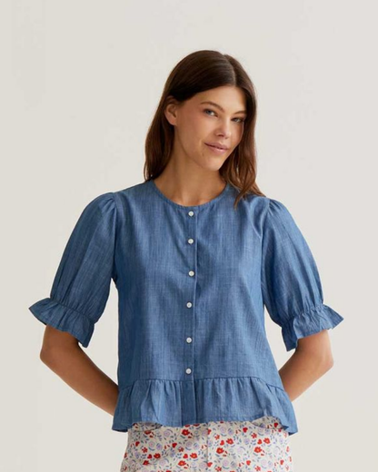 Woman wearing a blue denim blouse with ruffled sleeves on a plain background