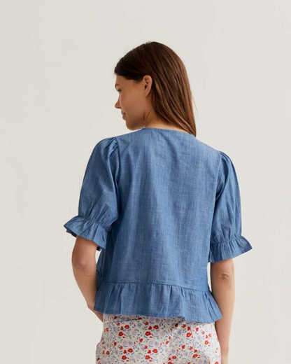 Woman wearing a blue denim top with ruffled sleeves on a plain background