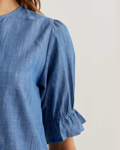 Blue denim-style top with ruffled sleeves on a plain background
