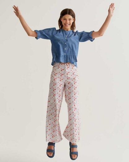 Woman wearing a blue shirt and floral pants with arms raised on a plain background