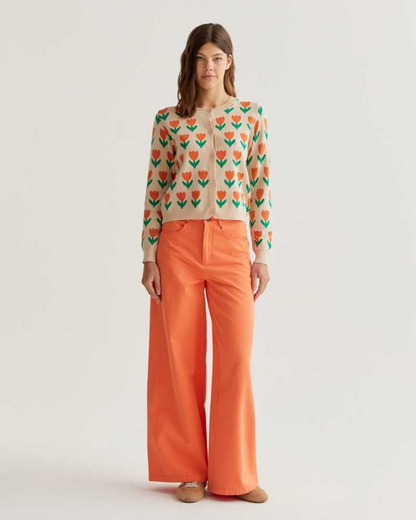 Woman wearing a patterned sweater and orange pants on a light gray background
