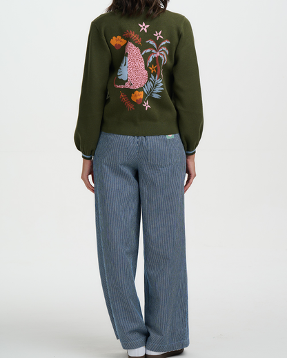 Person wearing a green sweater with a colorful design and blue pants on a white background