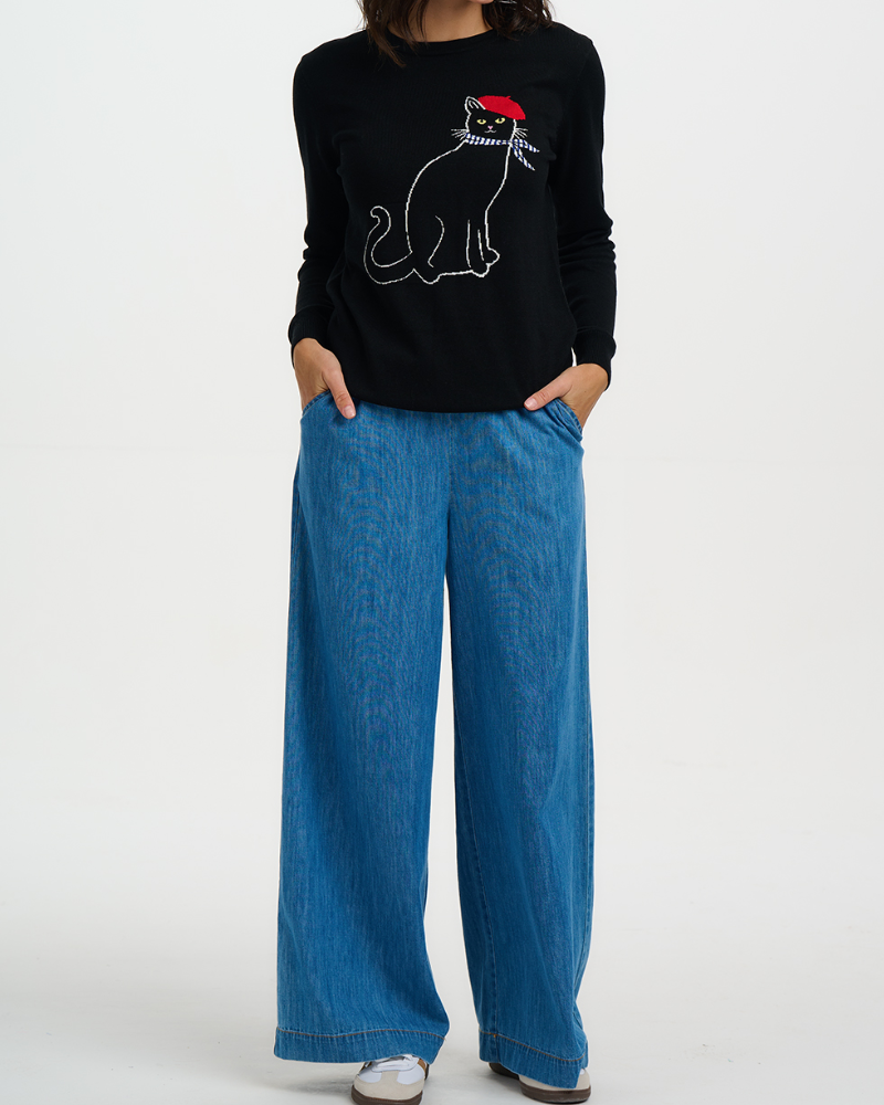Person wearing a black sweatshirt with a cat design and blue jeans on a white background