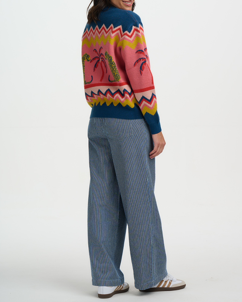Person wearing a colorful sweater with a geometric pattern and blue pants on a white background