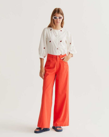 Person wearing a white blouse with red polka dots and red pants on a white background