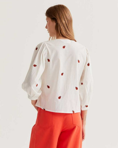 Woman wearing a white blouse with red patterns and red pants on a light background
