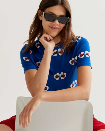 Woman wearing a blue shirt with ladybird patterns and sunglasses, sitting on a white chair against a light background.