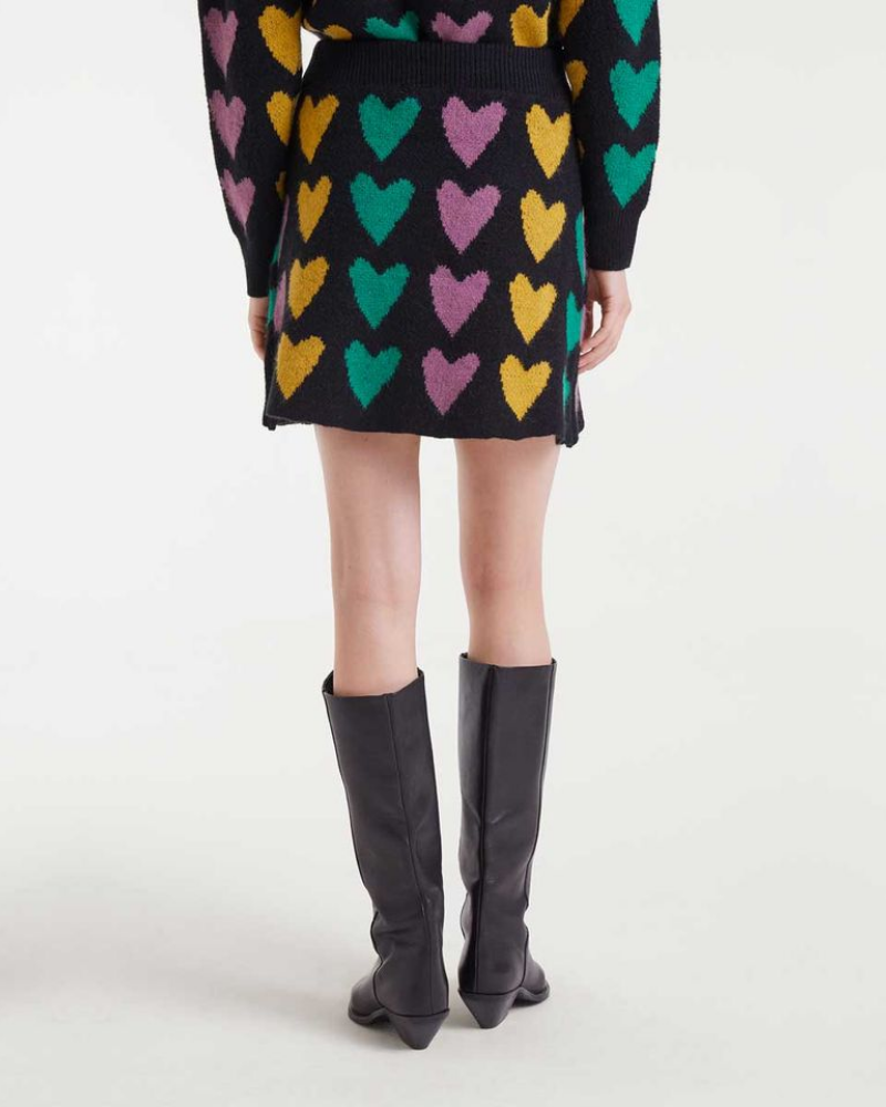 Person wearing a black skirt with colorful heart patterns and black knee-high boots on a white background