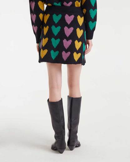 Person wearing a black skirt with colorful heart patterns and black knee-high boots on a white background