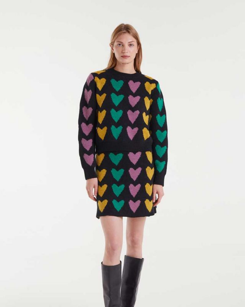 Woman wearing a black sweater with colorful heart pattern on a white background