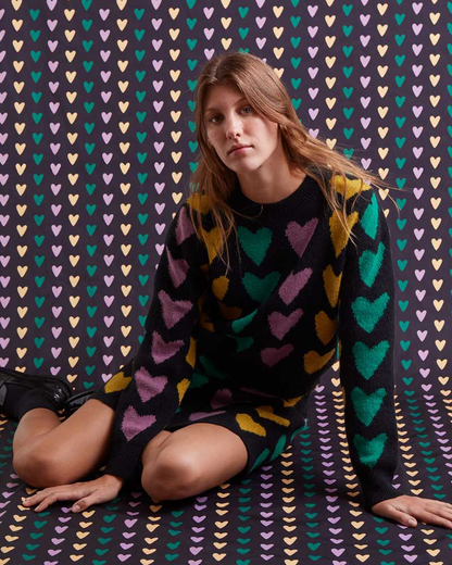 Woman wearing a colorful heart-patterned dress sitting on a patterned background