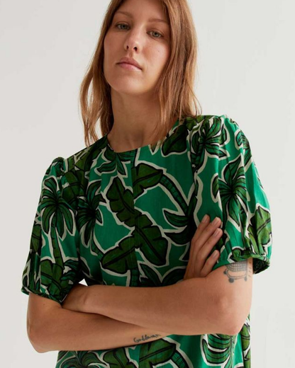 Woman wearing a green and black leaf-patterned top against a white background