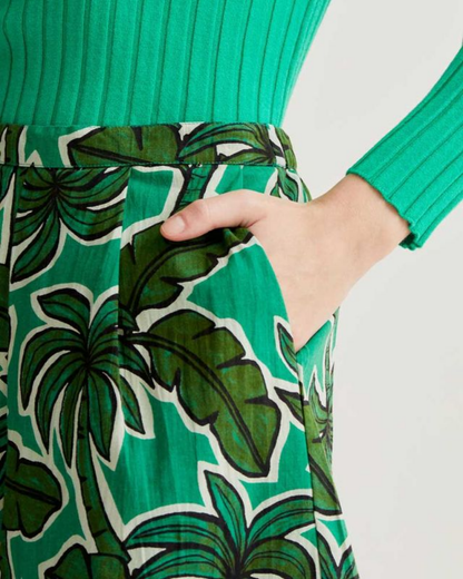 Green dress with tropical leaf pattern and a hand in the pocket against a white background