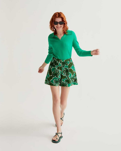 Woman wearing a green sweater and patterned shorts on a white background