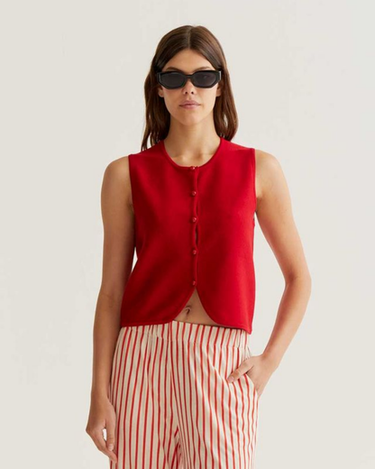 Woman wearing a red sleeveless top and striped pants on a plain background