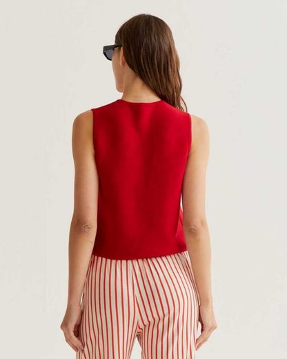 Woman wearing a red sleeveless top and striped pants on a plain background