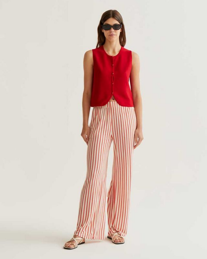 Woman wearing a red sleeveless top and striped pants on a white background