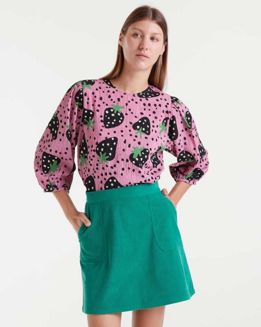 Woman wearing a pink blouse with black and green strawberry pattern and a green skirt on a white background