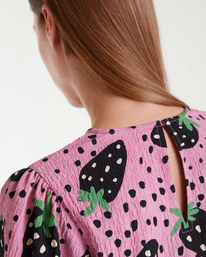 Close-up of a pink top with black strawberry pattern on a white background