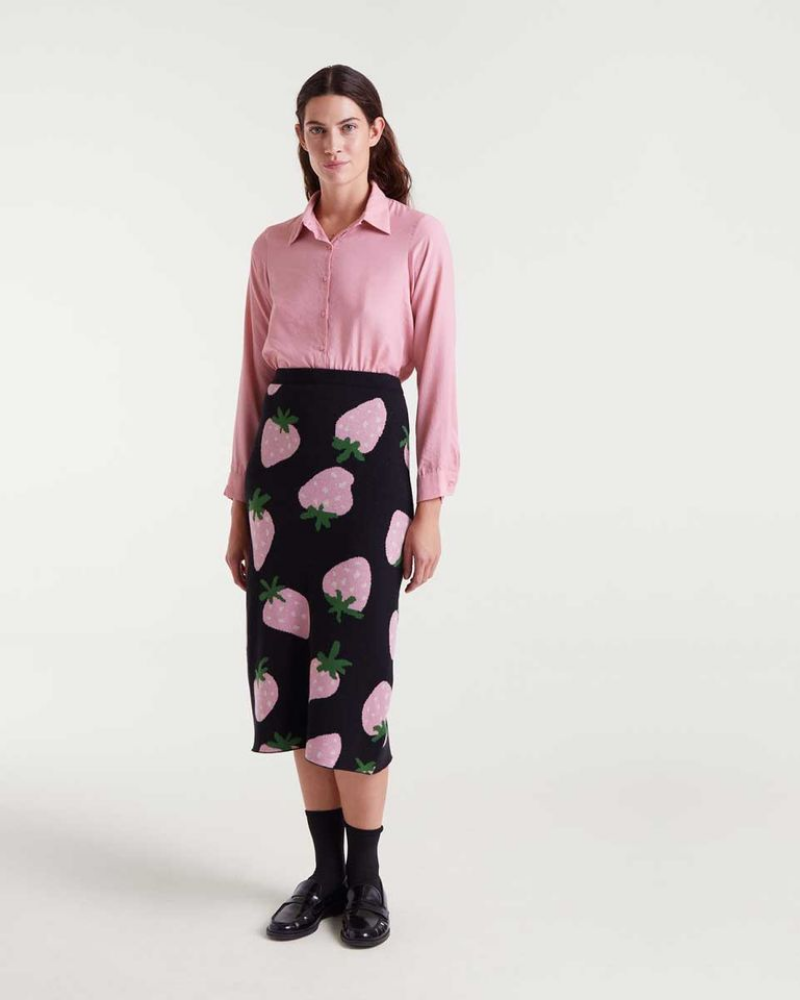 Woman wearing a pink shirt and black skirt with strawberry pattern on a white background