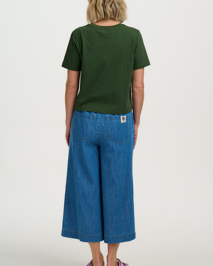 Person wearing a green t-shirt and blue denim pants on a white background